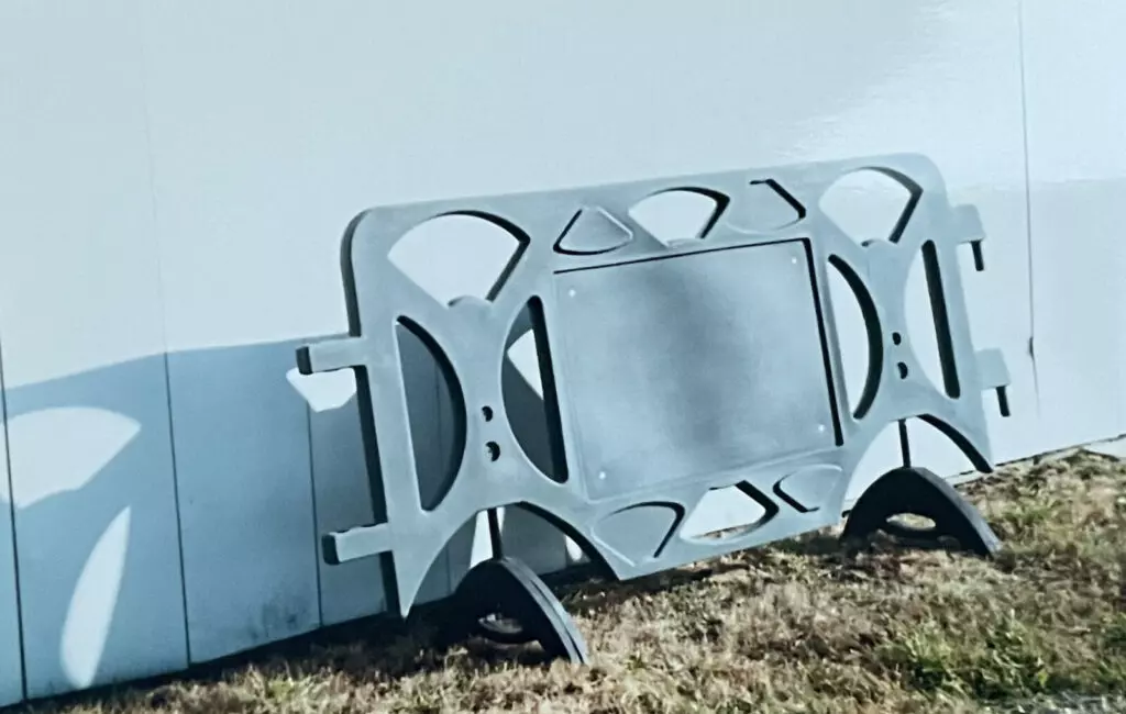 Image shows the very first version of the billboard barricade in gray, leaning up against a white wall on grass