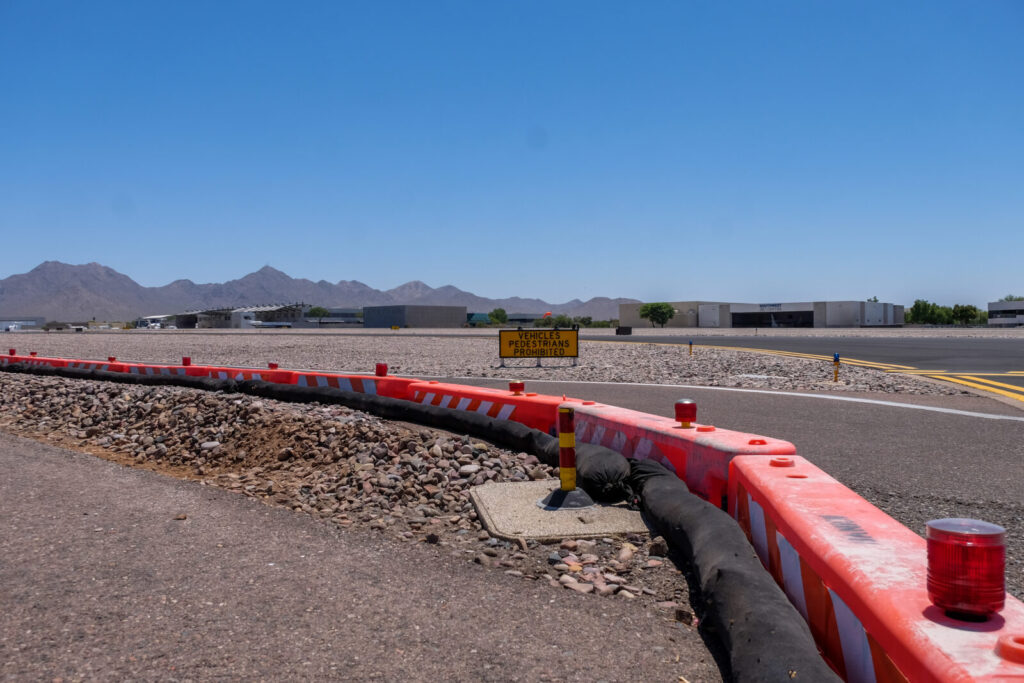 Orange OTW low-profile barricades with hazard lights line a runway airport work zone