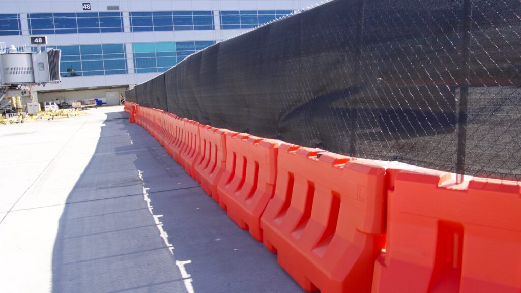 A line of orange OTW LCD barricades and fence panels with privacy mesh fade into the distance
