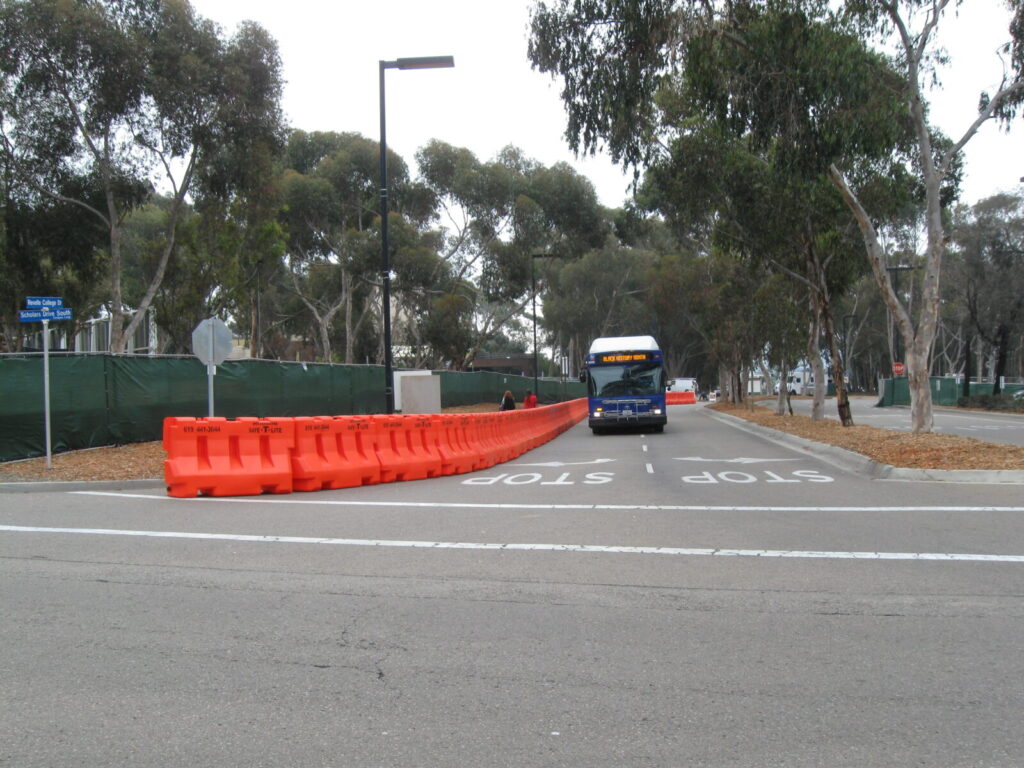 Line of MASH Tested OTW 42" Jersey Barriers lined up alongside road. Photo shows a bus driving towards camera. 