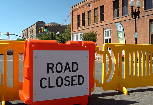 Road Closed wedge barricade with crowd control barricades in yellow behind.