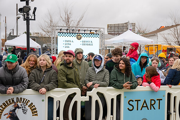 A crowd stands behind white OTW crowd barricades to watch the Doxie Derby in Millcreek, Utah