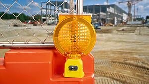 Example image: OTW Bidirectional Barricade Light mounted on an orange LCD jersey barricade fence panel in front of a large scale construction site
