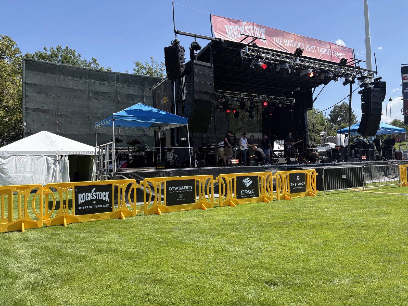 Yellow OTW Safety event barricades with black and white signage are set up in front of a large stage with a red awning.