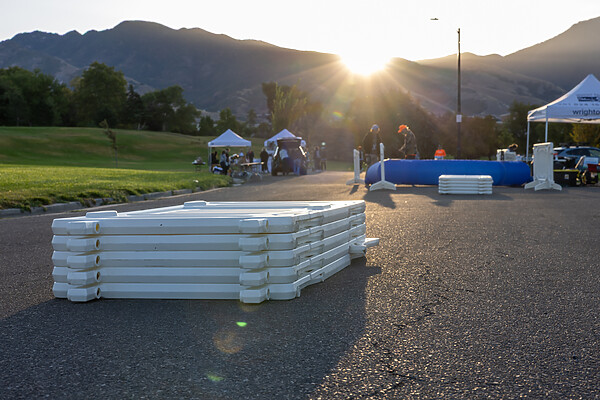 A stack of white OTw event barricades sit on a paved walkway waiting to be set up by volunteerts