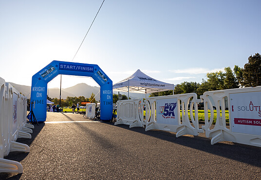 White OTW event barricades line both sides of a path directed toward an inflated arch for the finish line of the 2025 Flutie 5K