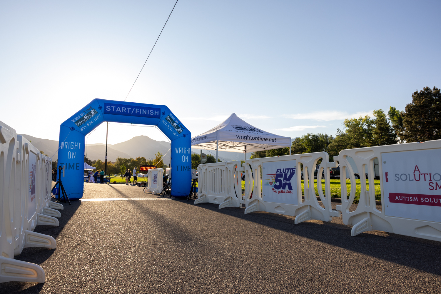 White OTW event barricades line both sides of a path directed toward an inflated arch for the finish line of the 2025 Flutie 5K