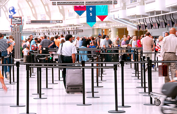 A queue of travelers lines up between stanchions while awaiting their turn at the airport