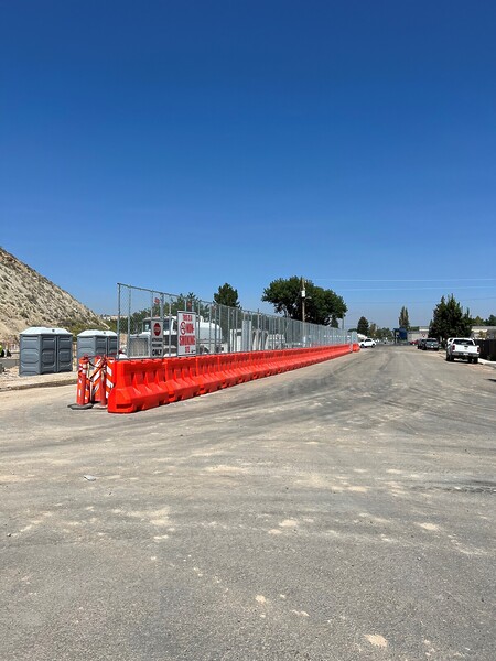 Orange construction barricades with added chain link fencing panels block off a construction site from a roadway
