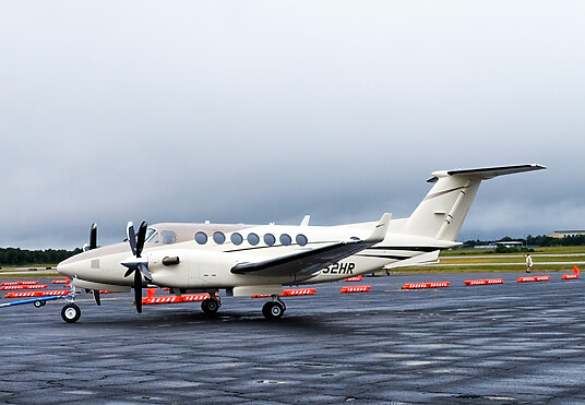 A small, white aircraft sits on a runway in front of spaced out orange low-profile barricades.