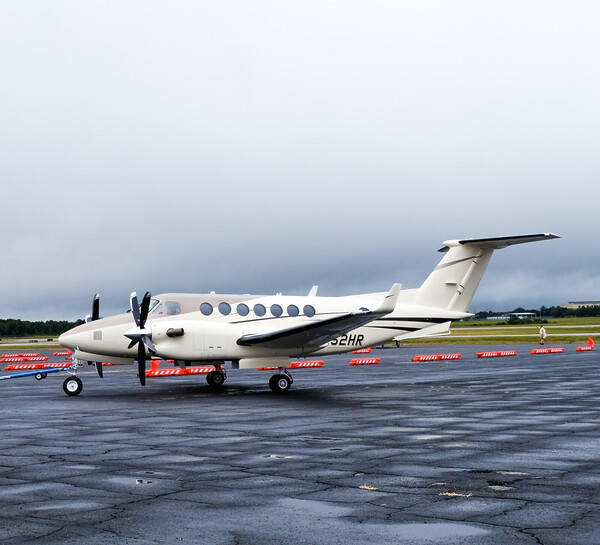 A small, white aircraft sits on a runway in front of spaced out orange low-profile barricades.