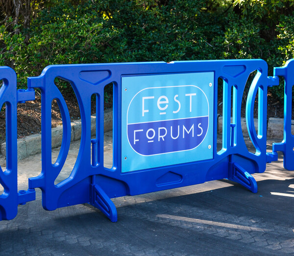 A royal blue pedestrian barricade sits in front of a curb. On the attached signage is a light blue and dark blue logo that says "Fest Forums"